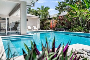 Ein Swimmingpool mit Liegestühlen und tropischer Bepflanzung.