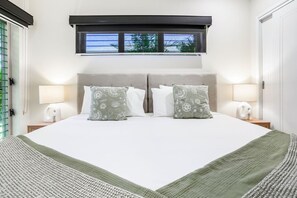 A neatly made bed with two pillows, a window above, and two bedside lamps. - Villa Jacana- Tropical 4BR Retreat in Port Douglas | Private Pool & Near Beach! (Port Douglas)