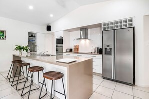 A modern kitchen with a central island, stainless steel appliances, and bar stools. - Villa Jacana- Tropical 4BR Retreat in Port Douglas | Private Pool & Near Beach! (Port Douglas)