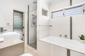 A modern bathroom with a glass-enclosed shower, a large white bathtub, and a vanity with a sink.