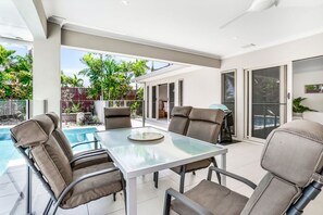 An outdoor patio with a glass table and chairs, a pool, and a view of the backyard.