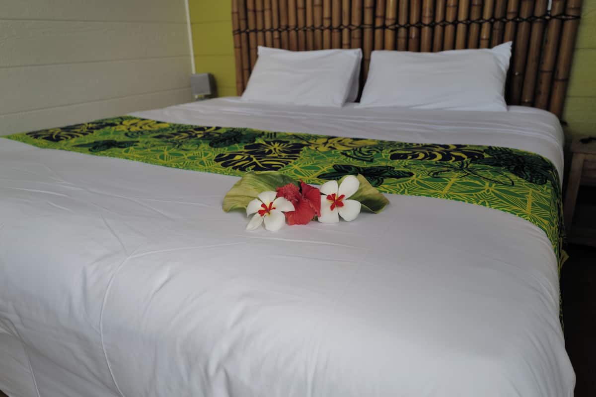A bed with white bedding, a green and yellow patterned bedspread, and a floral arrangement on the bed.