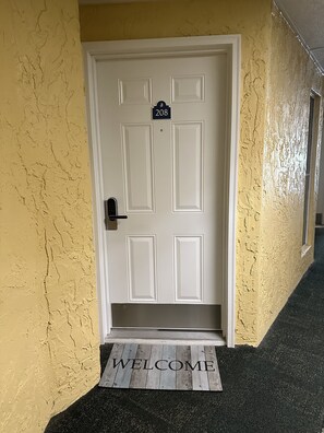 A white door with the number 208, a doormat with "WELCOME" written on it, and a textured yellow wall.