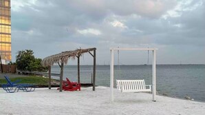 En strand med gyngestativ, hvid bænk og bindingsværkshus.