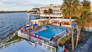 Et hotel med swimmingpool, udendørs siddepladser og udsigt til vandet.
