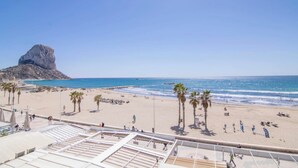 A beach with palm trees, a rocky outcrop, and the sea. - Calpe Playa | Arenal Bol Calpe (Calpe)
