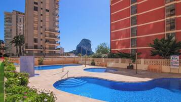 Un hotel con zona de piscina, varios balcones y vista a la montaña.