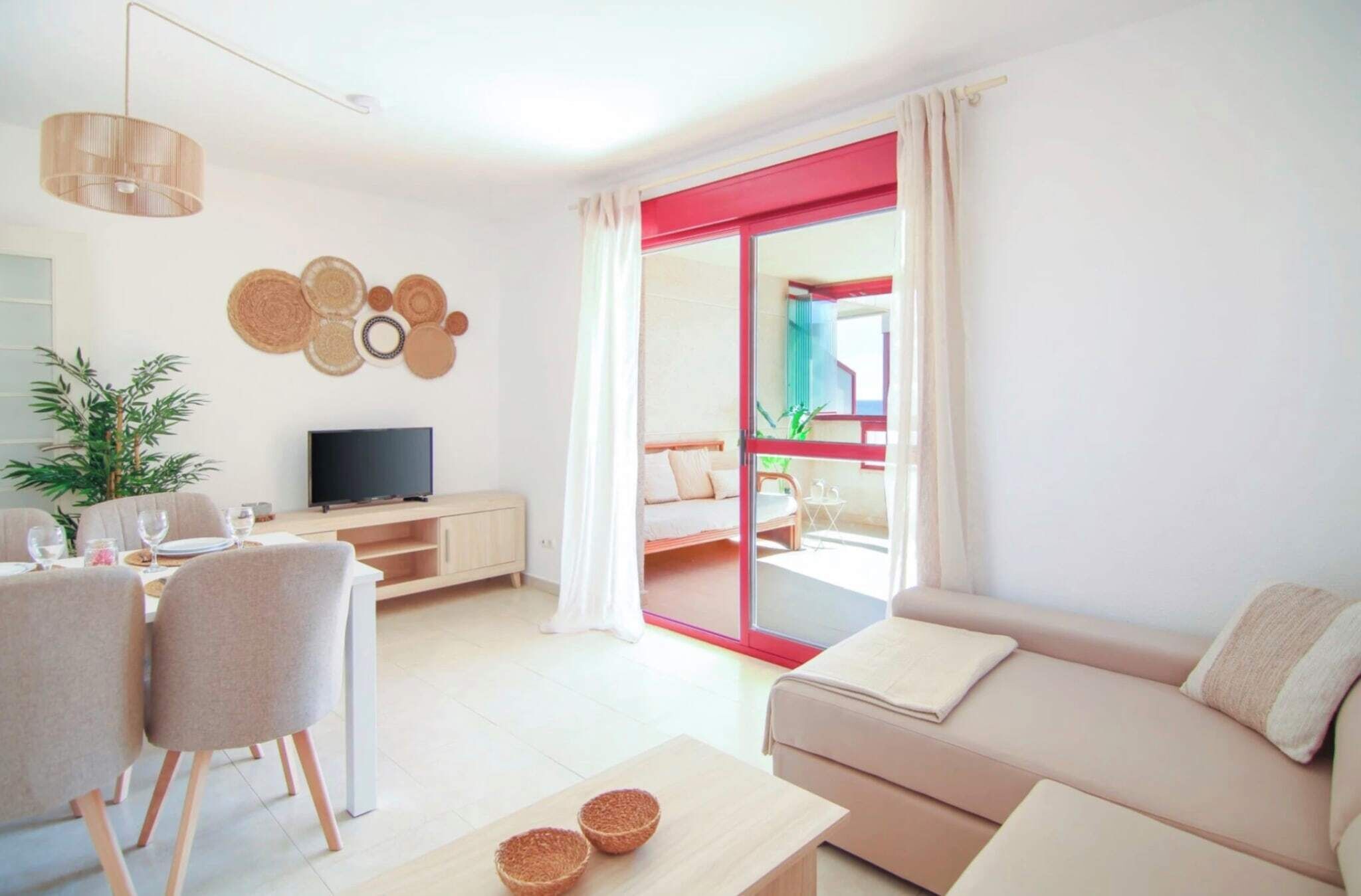 Una sala de estar moderna con sofá, comedor, televisión y un balcón con detalles en rojo.
