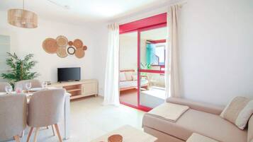 Una sala de estar moderna con sofá, comedor, televisión y un balcón con detalles en rojo.