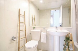 A bathroom with a toilet, sink, and mirror. There is a ladder leaning against the wall and a small plant on the sink.