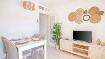 Un comedor moderno con una mesa blanca, sillas color beige y un televisor sobre un mueble de madera.
