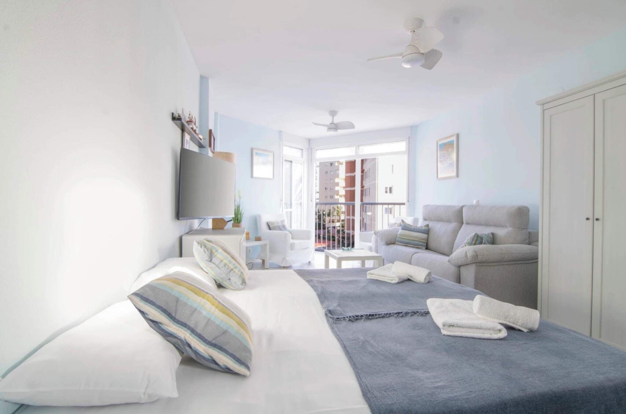 A modern bedroom with a bed, a sofa, a balcony, and a TV.
