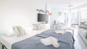 A bright hotel room with a large bed, a TV, a balcony, and a view of the city.