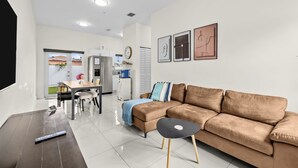 A modern living room with a brown sofa, a dining table, and a kitchen in the background. - Family & Friends Fun-Huge Yard -Games -BBQ-FirePit (Miami)