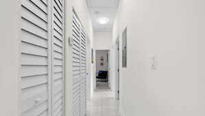 A narrow, white-walled hallway with a tiled floor, leading to a room with a bed and a desk. - Family & Friends Fun-Huge Yard -Games -BBQ-FirePit (Miami)