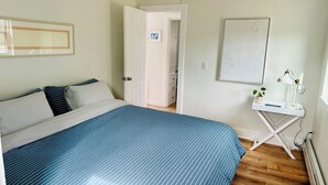 Un dormitorio con cama, escritorio, ventilador de techo y puerta que da a otra habitación.