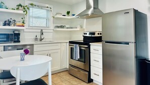 Cocina moderna con armarios blancos, estufa de acero inoxidable, refrigerador y ventana con persianas.