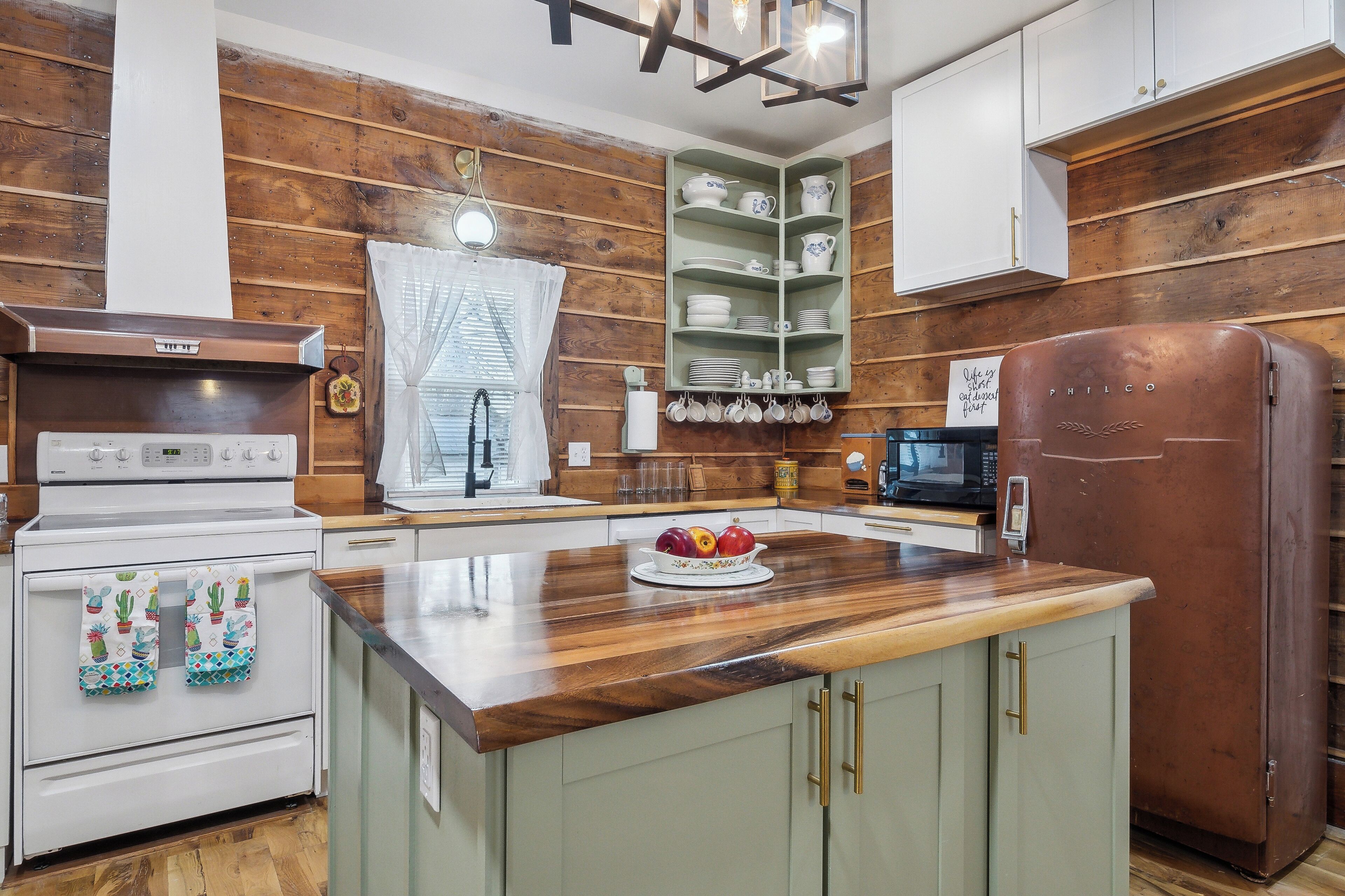 A kitchen with wooden paneling, a stainless steel stove, a brown refrigerator, and a wooden countertop with a fruit bowl.