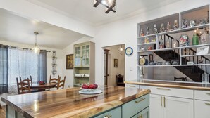 A kitchen with a wooden countertop, a dining area with chairs, and a shelf with various items. - 1800s Farmhouse—King Bed~Big Kitchen~Games & DVDs (Broken Arrow)