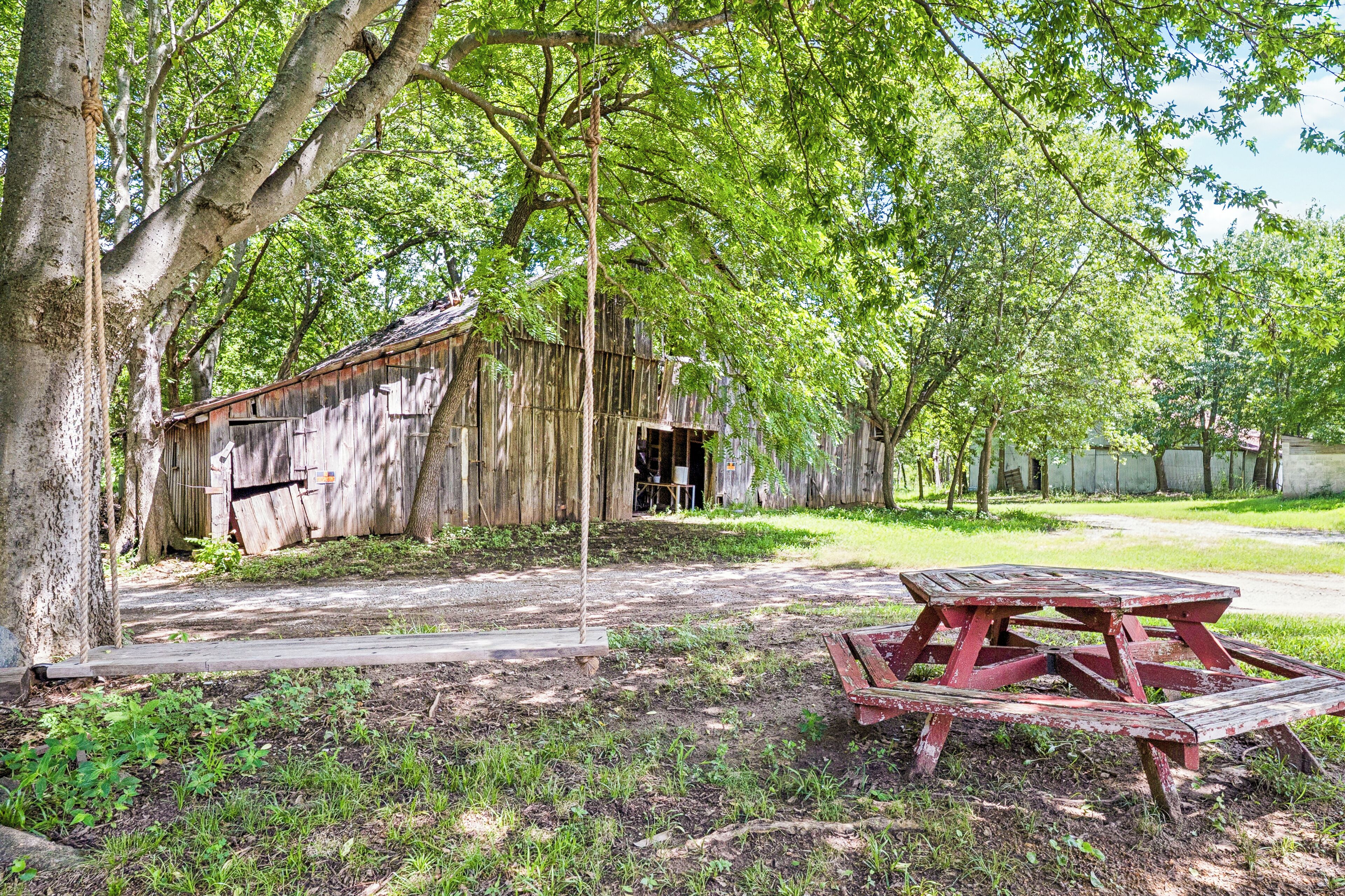 Une grange rustique en bois, avec un portique et une table de pique-nique, située dans une zone boisée.