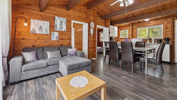Ein gemütliches Blockhauss-Interieur mit grauem Sofa, Esstisch aus Holz und Stühlen.