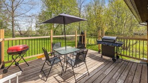Eine Holzterrasse mit einem Glastisch, zwei Stühlen, einem Grill und einem roten Schubkarren.