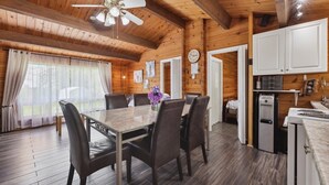 Ein Holzblockhaus-Interieur mit Esstisch, Stühlen, Deckenventilator, Küchenzeile mit Schränken und Wasserspender.