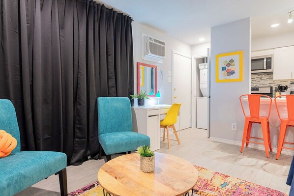 A modern living room with teal and orange chairs, a wooden coffee table, and a black curtain.