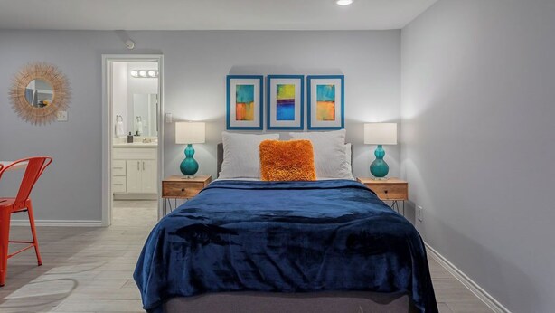 A bedroom with a bed, two nightstands, a red chair, a mirror, and three framed artworks on the wall. - Montrose Amble Studio! Medical Center 02 ★★★★★ (Houston)