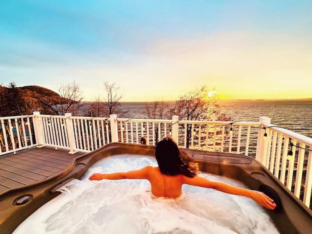 Una persona si rilassa in una vasca idromassaggio ammirando il tramonto su un lago.