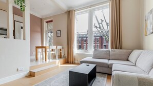 Een moderne woonkamer met een grijze bank, een zwarte salontafel en een uitzicht op gebouwen door grote ramen.