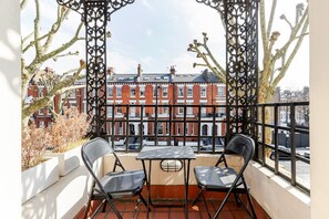 Enjoy the view from this balcony with a red-brick building in the background, featuring a metal railing and a small table for two.