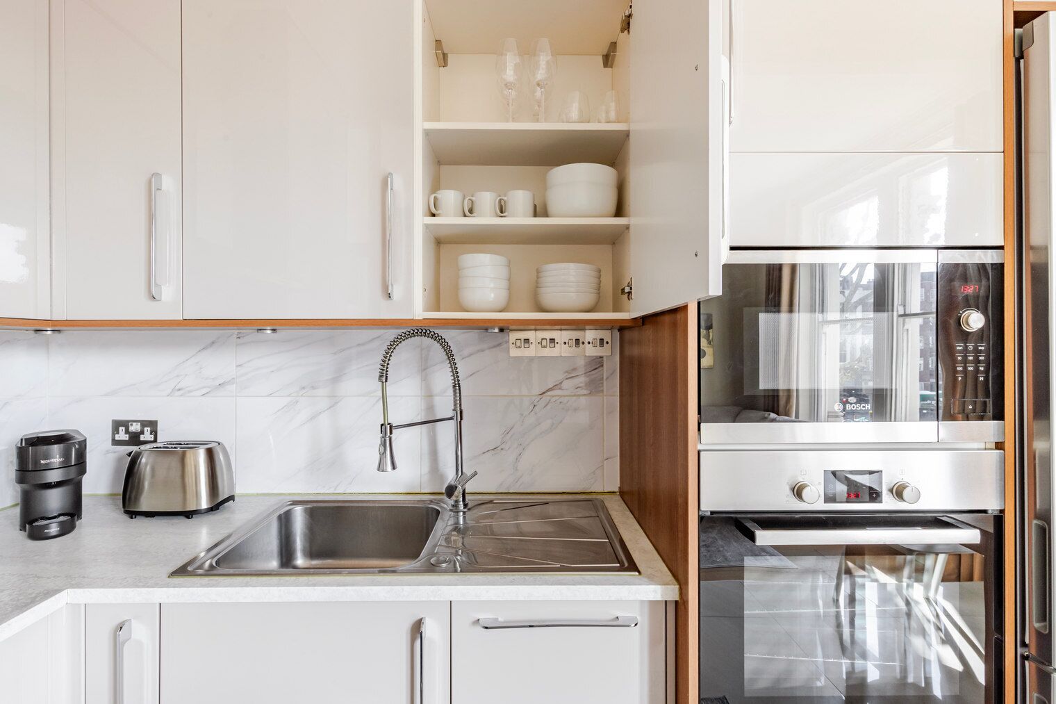 A modern kitchen with white cabinets, a stainless steel sink, a Bosch oven, and a toaster.