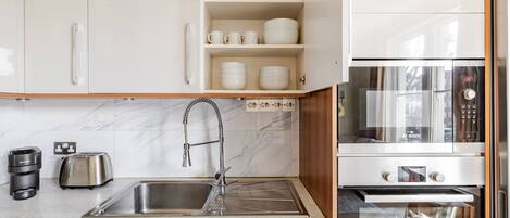 A modern kitchen with white cabinets, a stainless steel sink, a Bosch oven, and a toaster.