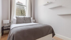 Een moderne slaapkamer met een bed, nachtkastjes, een raam met gordijnen en ingebouwde planken.