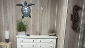A room with a white dresser, a starfish decoration, a turtle decoration, a seahorse decoration, a potted plant, and a patterned carpet. - Lucky Enough! Adorable apartment sleeps 5, no cleaning fee/ free beach parking! (Emerald Isle)