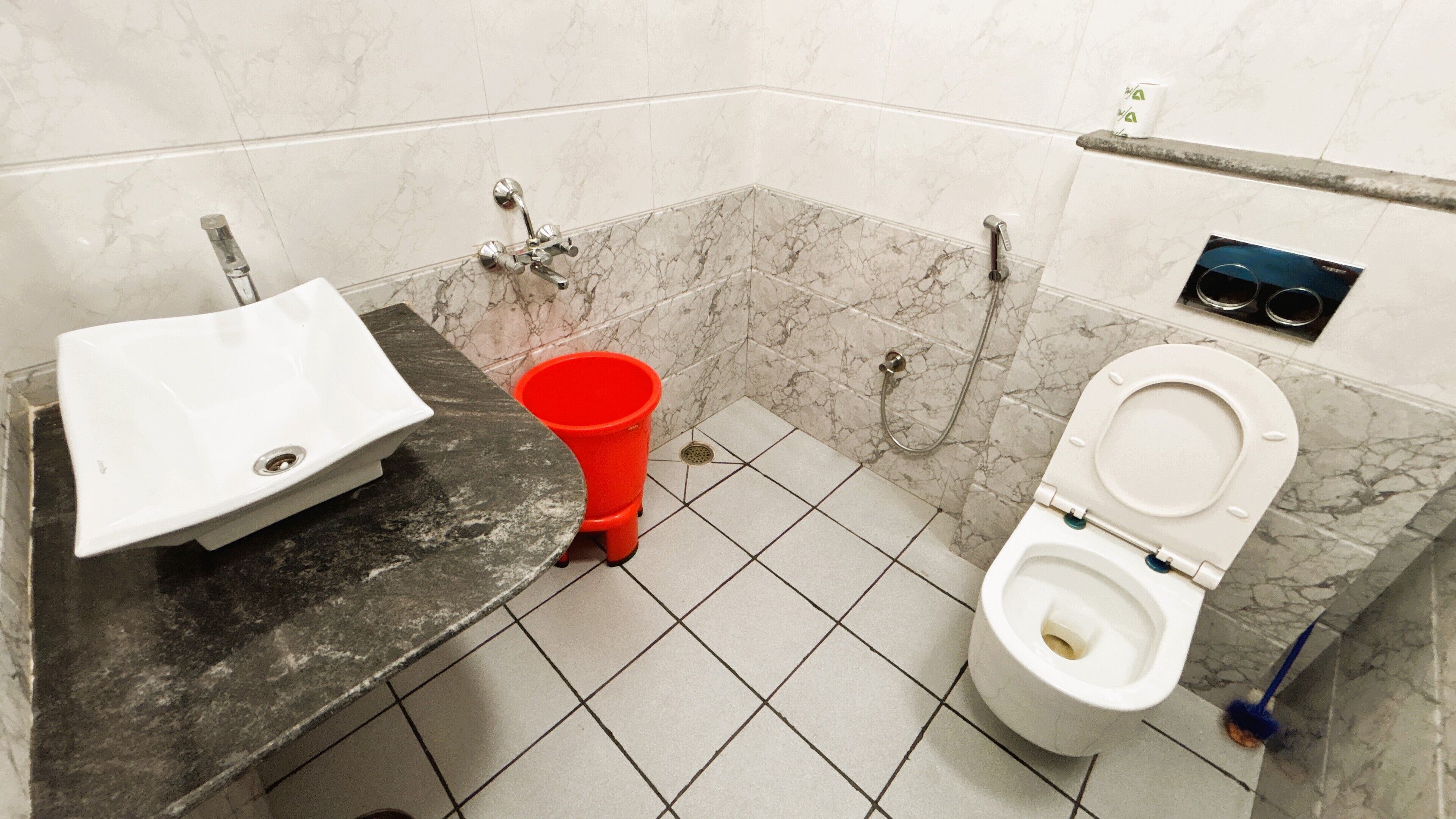 Un baño con un lavabo blanco, un cubo rojo, un inodoro y una zona de ducha.
