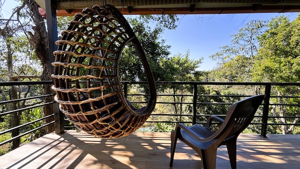 A hanging chair on a balcony with a view of trees and a clear sky. - Hong Sau Resort (Sakleshpur)