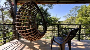 Uma cadeira suspensa numa varanda com vista para árvores e um céu limpo.
