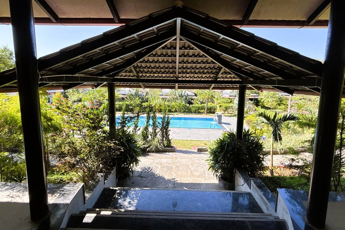 A covered outdoor area with a pool, surrounded by greenery and a clear view of the pool.