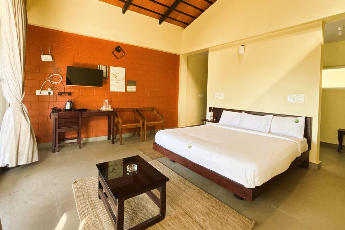 A hotel room with a large bed, a desk with a chair, a small table, and a TV on the wall.