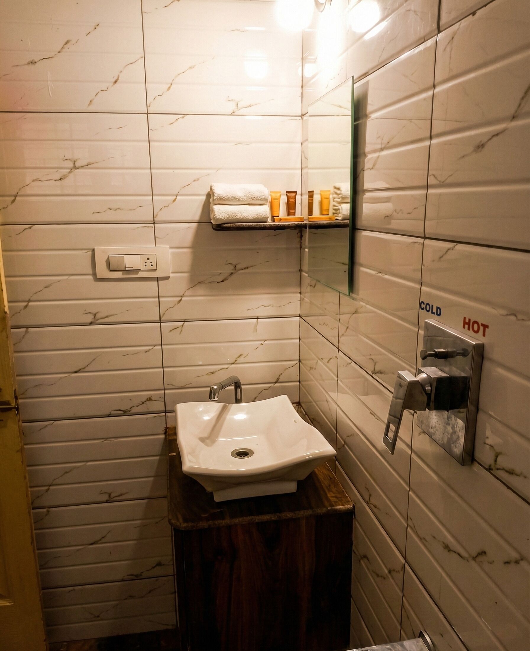 A bathroom with a white sink, marble-patterned walls, a towel rack, and a mirror with a temperature control sign.
