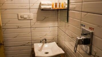 A bathroom with a white sink, marble-patterned walls, a towel rack, and a mirror with a temperature control sign.