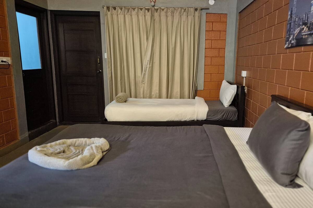 A hotel room with two beds, a brick wall, a cityscape poster, and a door with a light switch.