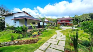 Two modern houses with red roofs and white walls, surrounded by lush greenery and a stone pathway. - Hong Sau Resort (Sakleshpur)