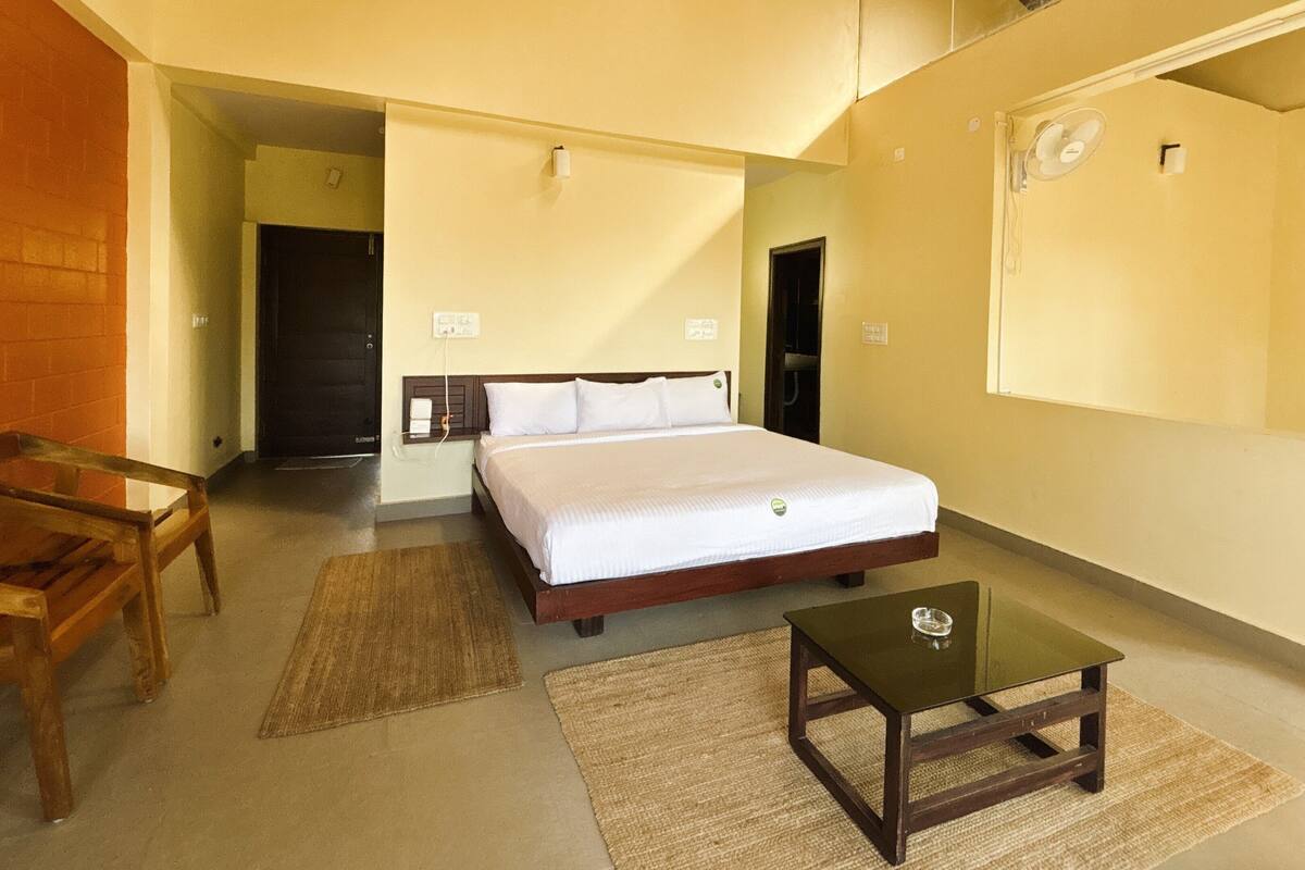 A bedroom with a bed, a wooden chair, a glass table, and a small rug.
