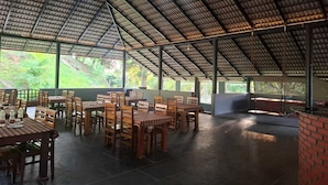 An indoor dining area with tables and chairs, large windows, and a high ceiling. - Hong Sau Resort (Sakleshpur)