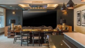 Een moderne eetruimte met een lange tafel en stoelen, verlichting boven en een grote flatscreen televisie.