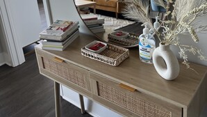 Een houten bureau met een spiegel, boeken, een flesje handdesinfectiemiddel en een vaas met gedroogde planten.