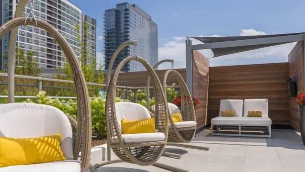 Buiten zitplaatsen met rieten stoelen en kussens, een houten pergola en uitzicht op stadsgebouwen.